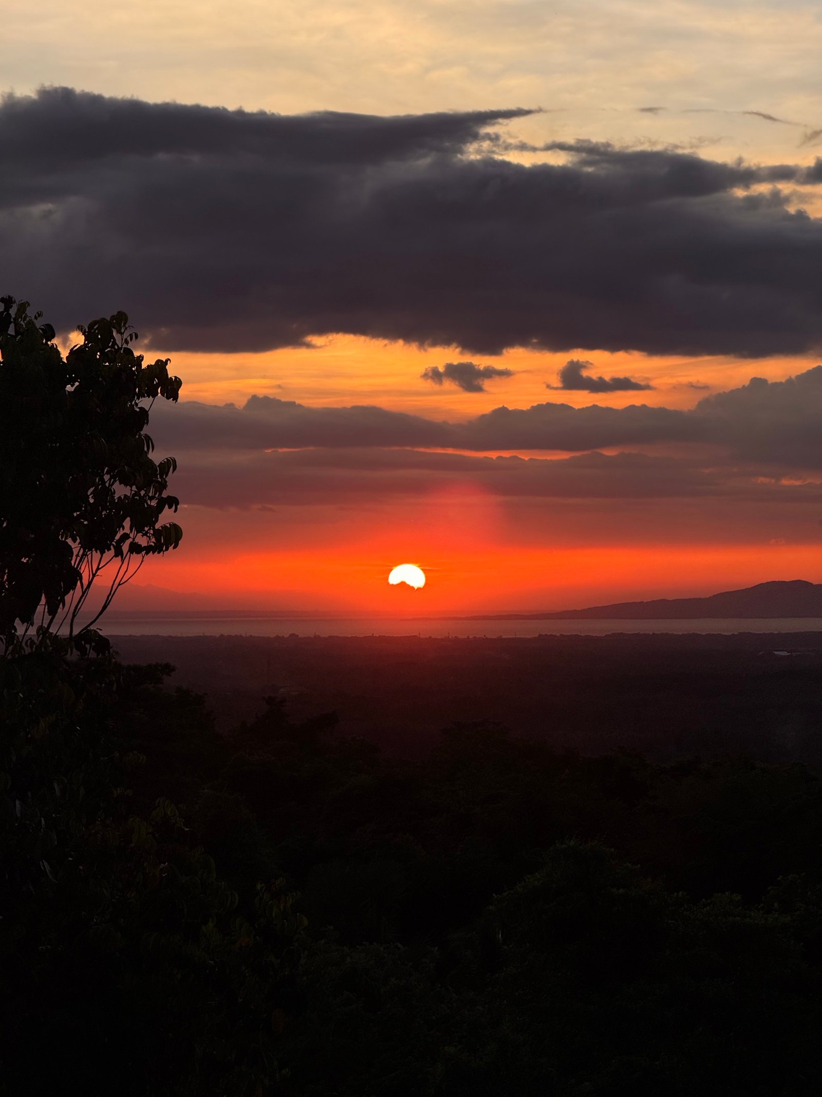 The sun setting blood-orange over the lowlands, seen from the ridge